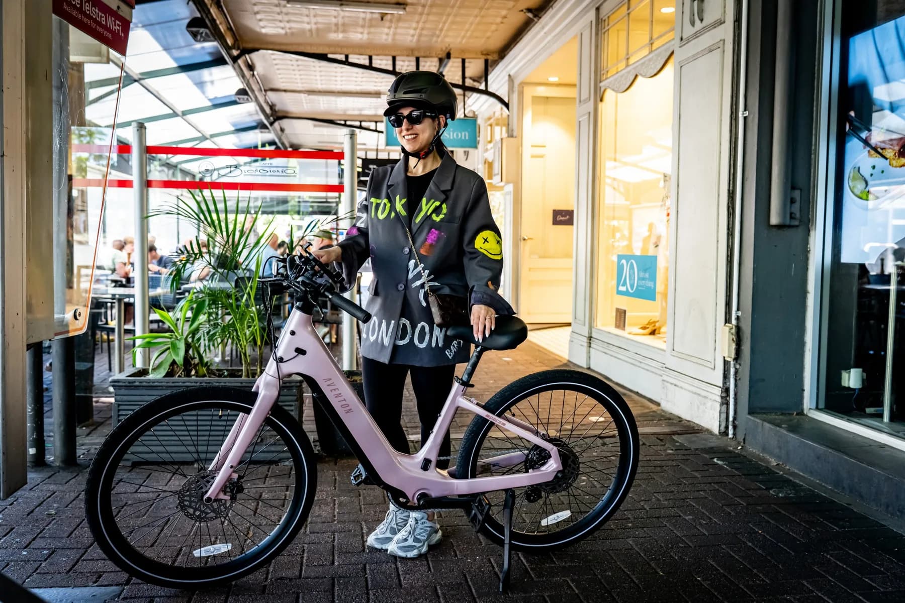Rider standing with a pink Aventon Pace 5 REC ST outside a cafe arcade