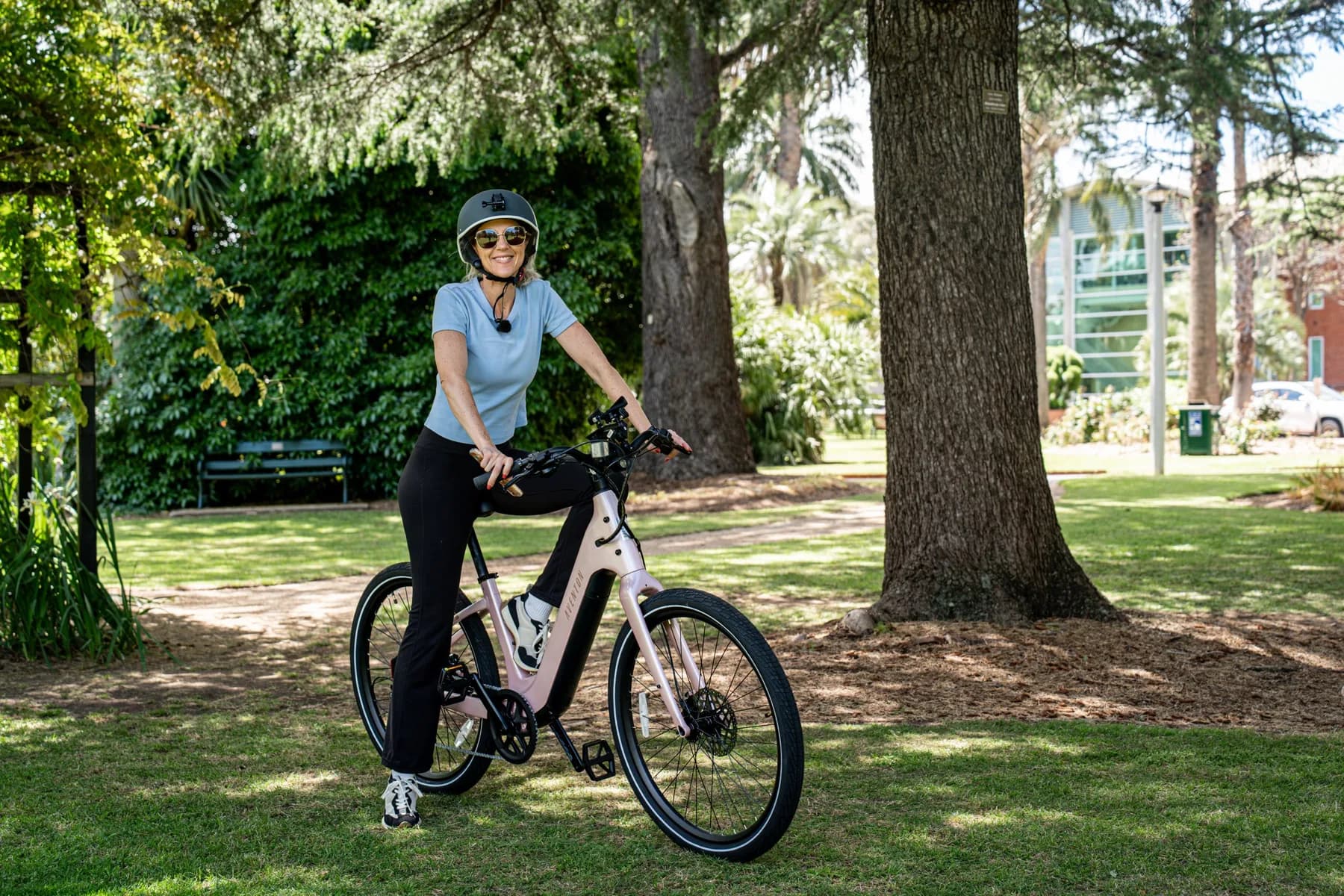 Rider in a helmet and sunglasses smiling on a pink Aventon Pace 5 REC ST on the grass in a park
