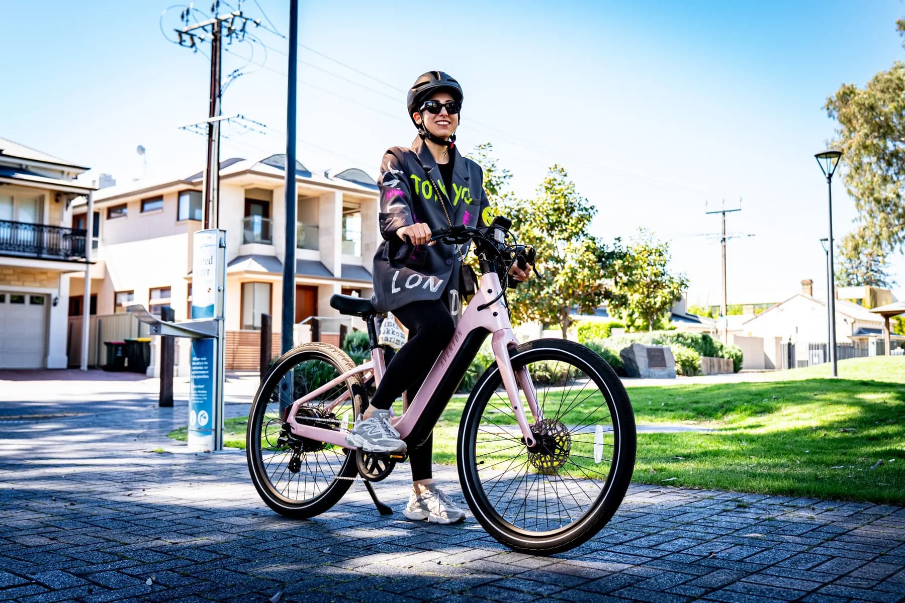 Rider smiling on a pink Aventon Pace 5 REC ST step-through e-bike on a paved footpath on a sunny day